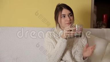 一个年轻的女孩穿着一件舒适温暖的毛衣在冬天的晚上在家喝茶，想些什么